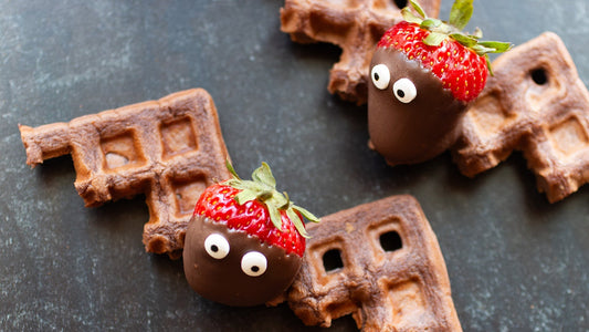 Halloween bat-shaped waffles made with Heavenly Waffles Chocolate Espresso mix, decorated with chocolate-covered strawberries and candy eyes.