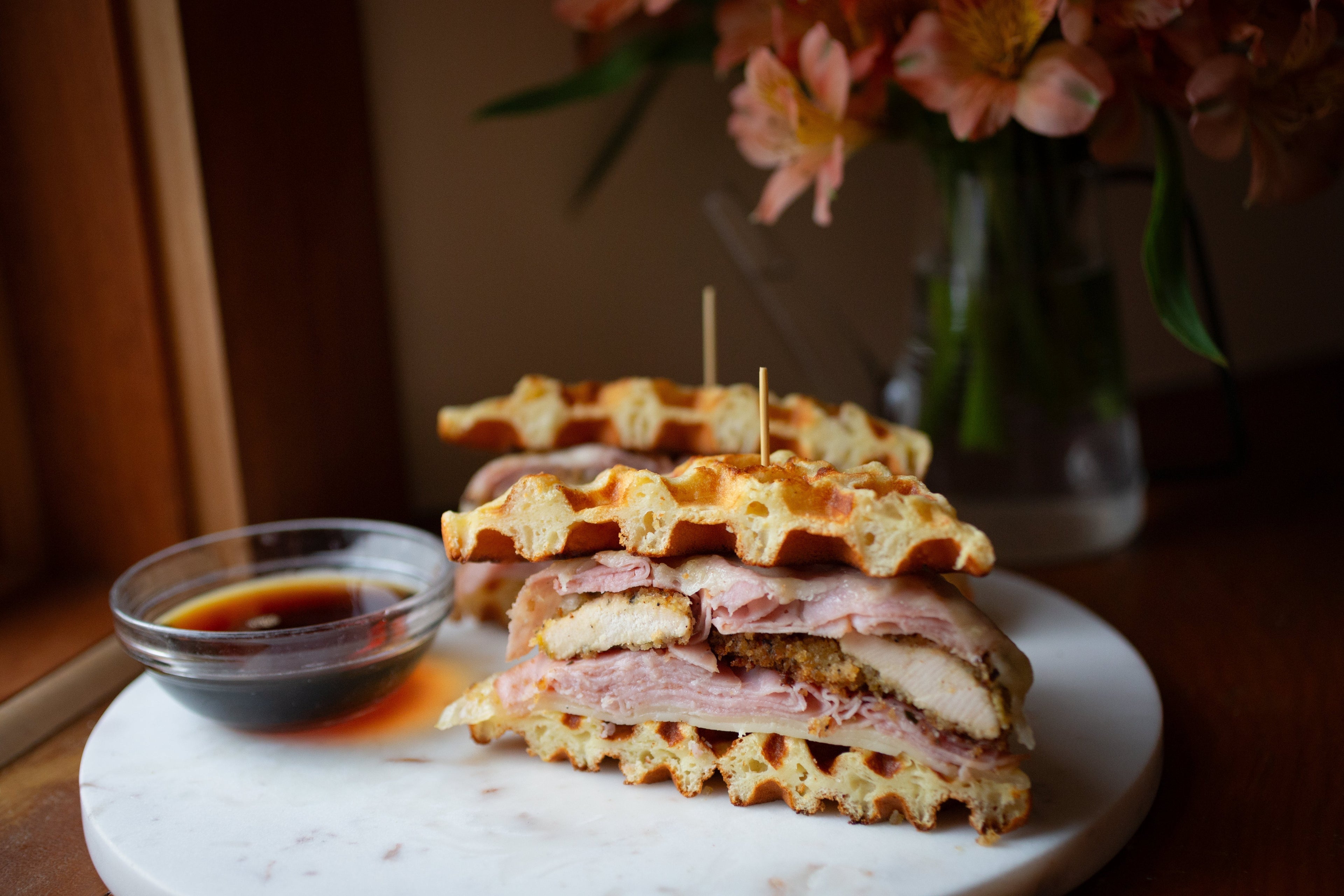 Chicken Cordon Bleu waffle sandwich made with crisp Heavenly Waffles, melted Swiss cheese, uncured ham, and breaded chicken, sliced and served with dipping sauces.