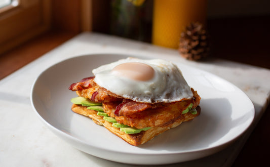 Savory breakfast stack on a Heavenly Waffle with hashbrowns, bacon, egg, avocado, and hot sauce