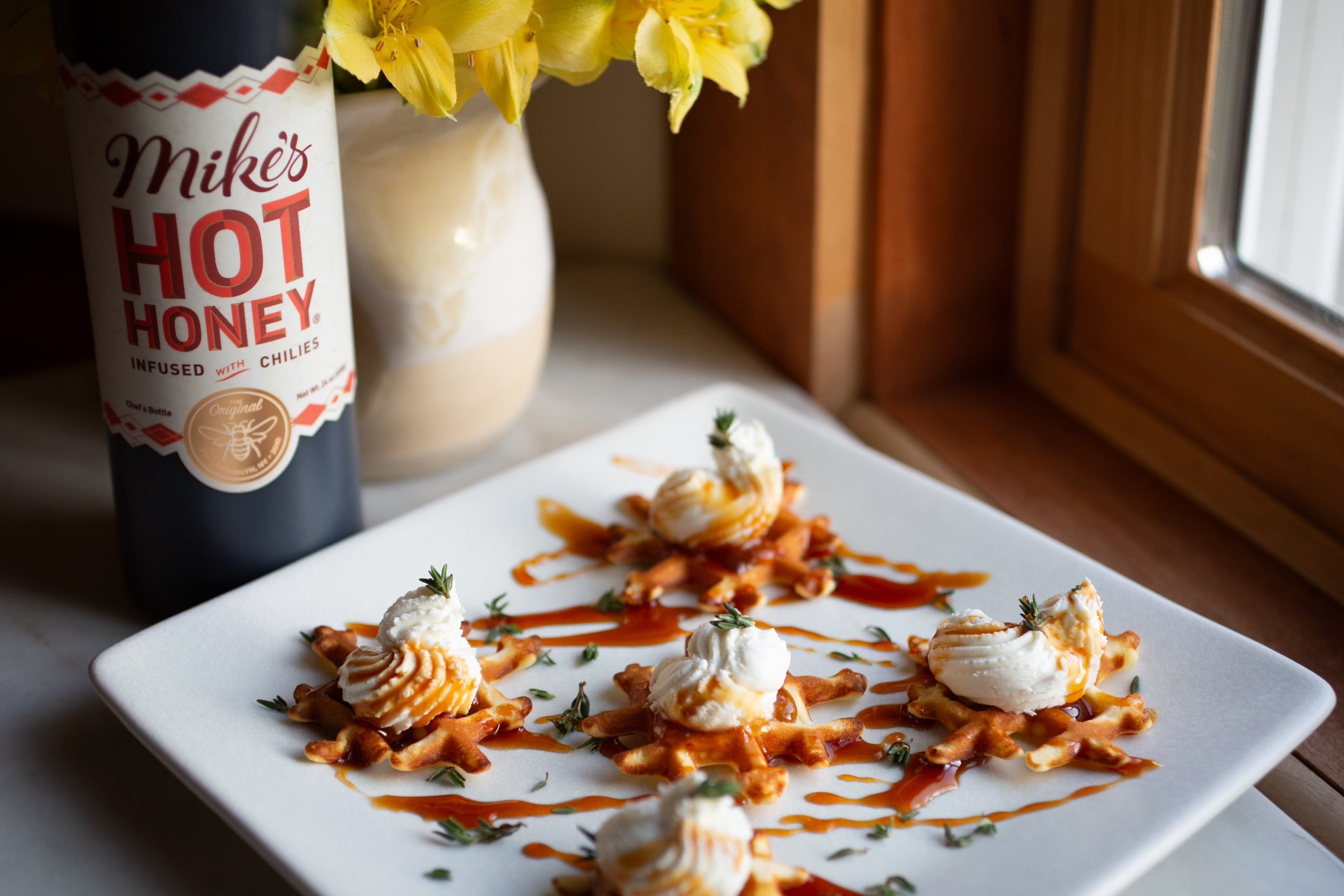 Protein-packed waffle bites topped with fig jam, piped goat cheese, fresh thyme, and hot honey on a serving platter.