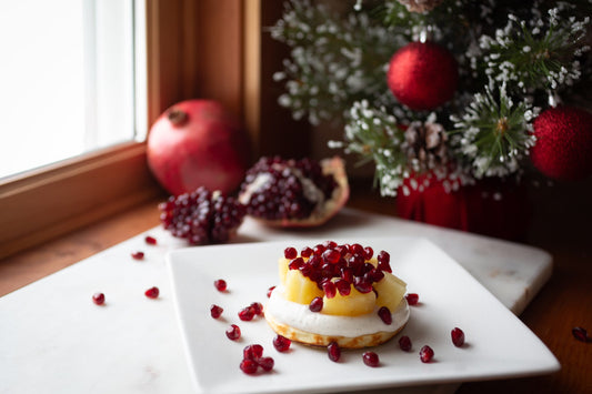 Protein waffles topped with vanilla Greek yogurt, fresh pineapple chunks, and pomegranate seeds on a white plate.